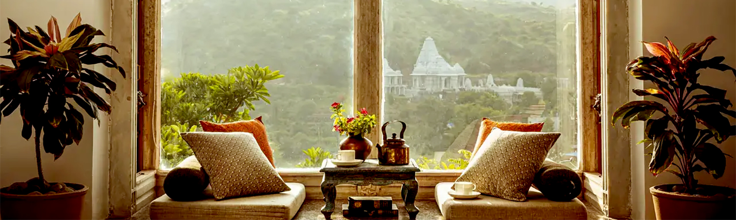 Blog 54 Two cushioned chairs and a small table with a teapot sit by a window framing a scenic view of hills and a distant temple—a perfect setting for your next reflective blog post.