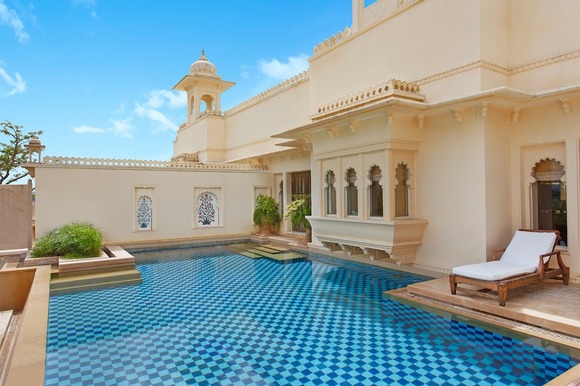 Luxurious outdoor pool with a patterned blue tile design, surrounded by a cream-colored building with ornate windows and a lounge chair, exemplifying one of the best destination wedding resorts in India.